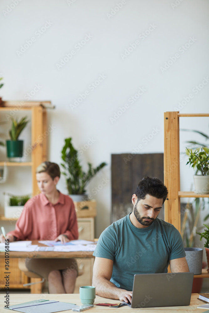 Vertical portrait of modern bearded man using laptop while working at wooden desk in office, copy space Vertical portrait of modern bearded man using laptop while working at wooden desk in office, copy space