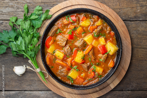 Obraz na plátně Goulash, beef stew or bogrash soup with meat, vegetables and spices in cast iron pan on wooden table