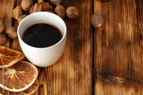 Cup of coffee with nutmeg and dried orange on brown wooden table