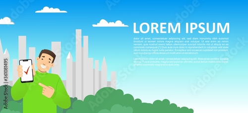 smiling guy with a phone on the background of the city, skyscrapers; shows the screen of the phone, points to it with a finger; red check mark on the screen; copy space horizontal, flat