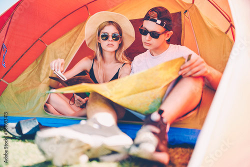 Romantic couple of travelers sitting in tent discussing route for hiking recreating during summer vacations together hipsters talking about destination using map camping during journey adventure