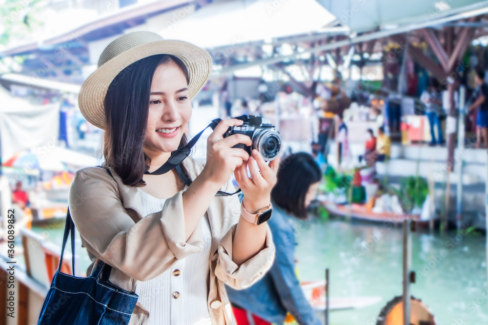 asia female tourists wearing hat holding camera and smartphone take photo vlog live. Beautiful woman take taxi boat visiting Damnoen Saduak floating market,Ratchaburi.