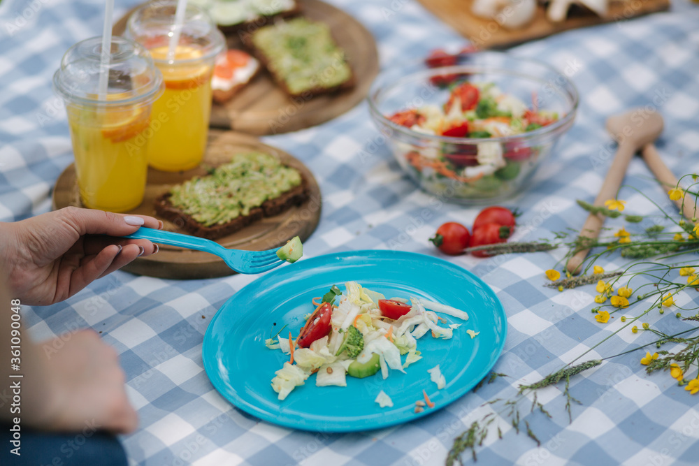 Woman take salad from blue plate on vegan picnic outdoors. Fresh and healthy food Woman take salad from blue plate on vegan picnic outdoors. Fresh and healthy food