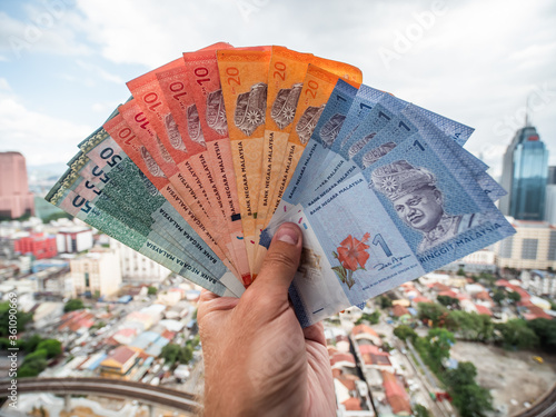 A young man holds in his hands the money of Malaysia against the background of the city center of Kuala Lumpur. photo