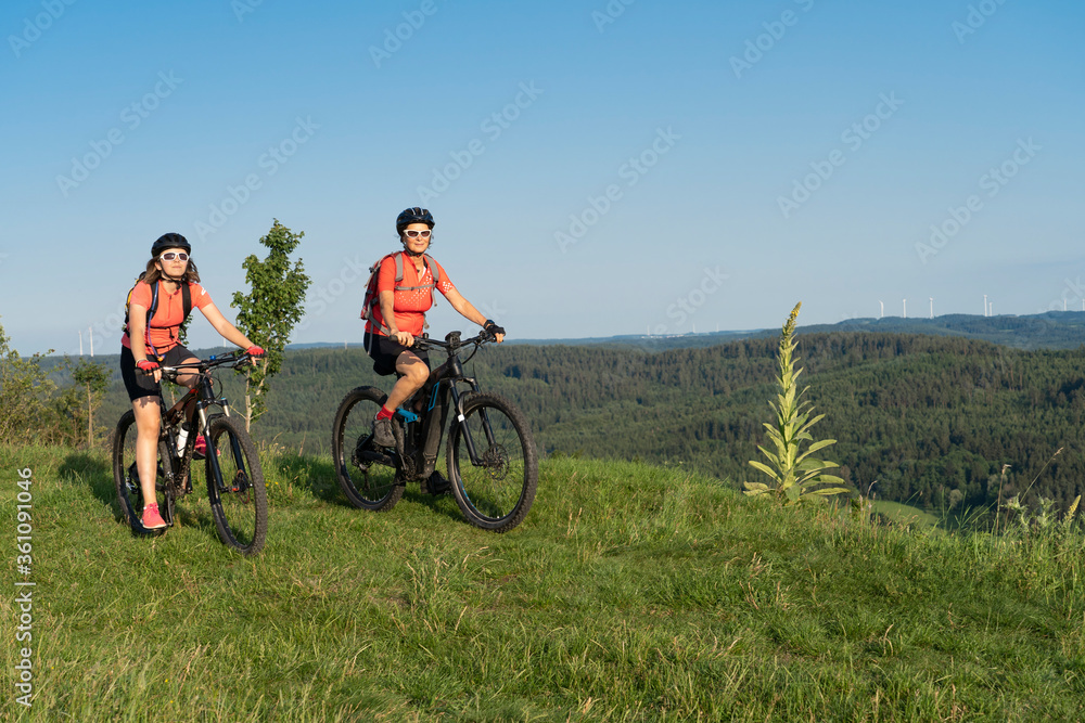 Fototapeta premium Grandmother with electric mountain bike and granddaughhter without electric help on a smooth meadow trail in the Franconian Switzerland area of Bavaria, Gemany