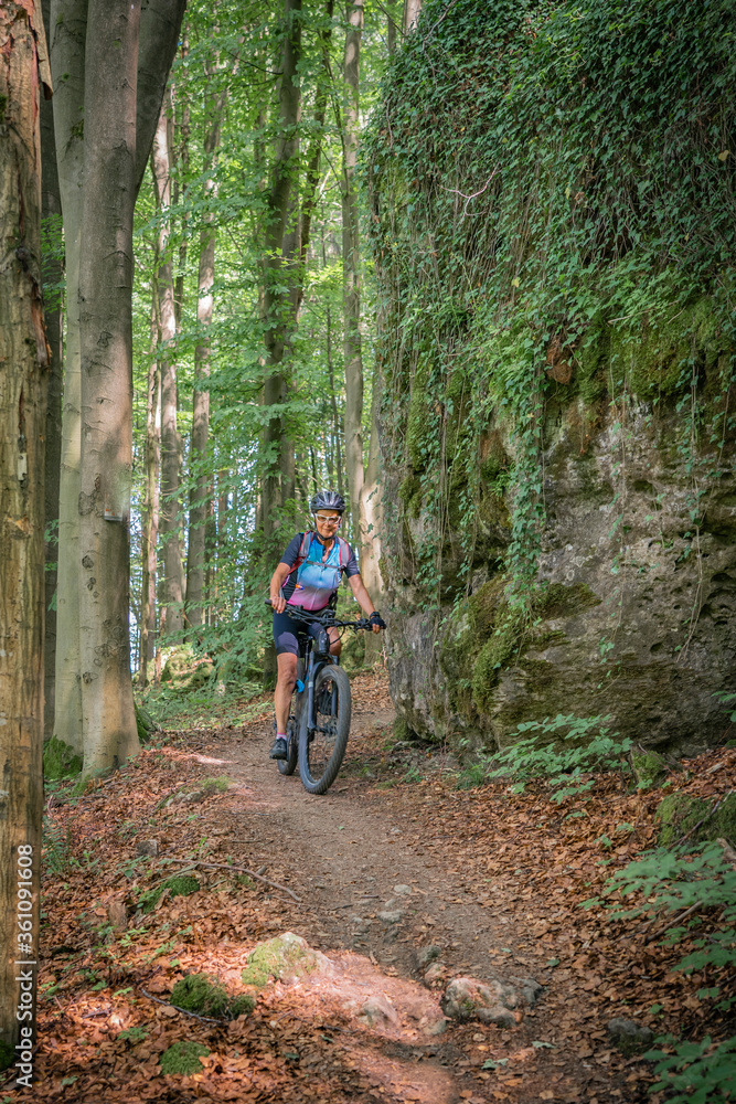 pretty senior woman underway on her electric mountain bike on a rocky forest trail in Franconian Switzerland, Bavaria, Germany pretty senior woman underway on her electric mountain bike on a rocky forest trail in Franconian Switzerland, Bavaria, Germany