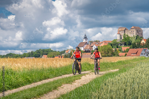 grandmother and granddaughter riding their mountain bikes in front of the awesome skyline of Hiltpoltstein in Frankonian Switzerland, Bavaria, Germany