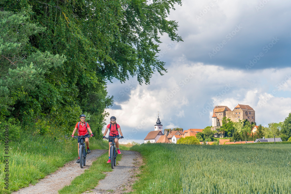 Fototapeta premium grandmother and granddaughter riding their mountain bikes in front of the awesome skyline of Hiltpoltstein in Frankonian Switzerland, Bavaria, Germany