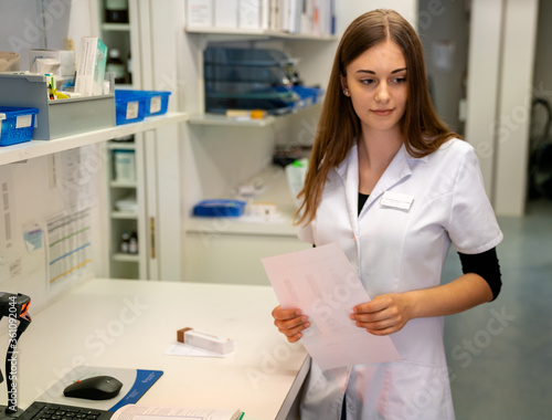 Wallpaper Mural young attractive female pharmacy employee holds paper with medical information in a pharmacy Torontodigital.ca