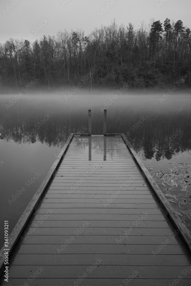View of a fishing dock extending into a calm, foggy pond in early morning