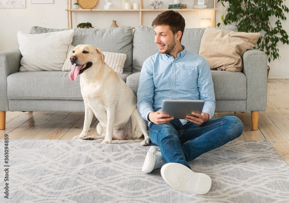 Young man at home with a tablet and labrador Young man at home with a tablet and labrador