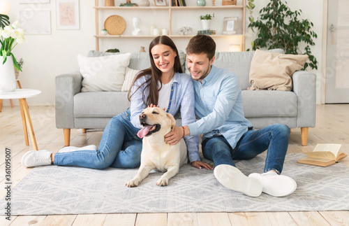 Young happy couple with dog sitting in living room