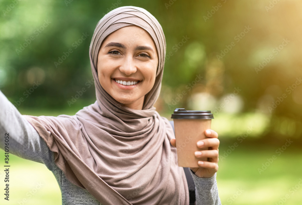 Cheerful girl in hijab taking selfie while drinking coffee outdoor Cheerful girl in hijab taking selfie while drinking coffee outdoor