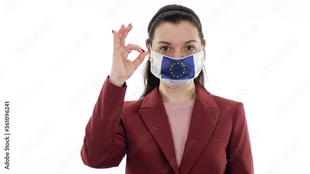 Virus and disease prevention concept. Pandemic and quarantine. A woman wears a protective medical mask with the image of the flag of Europe, European Union. Woman shows a ring or ok gesture. Virus and disease prevention concept. Pandemic and quarantine. A woman wears a protective medical mask with the image of the flag of Europe, European Union. Woman shows a ring or ok gesture.
