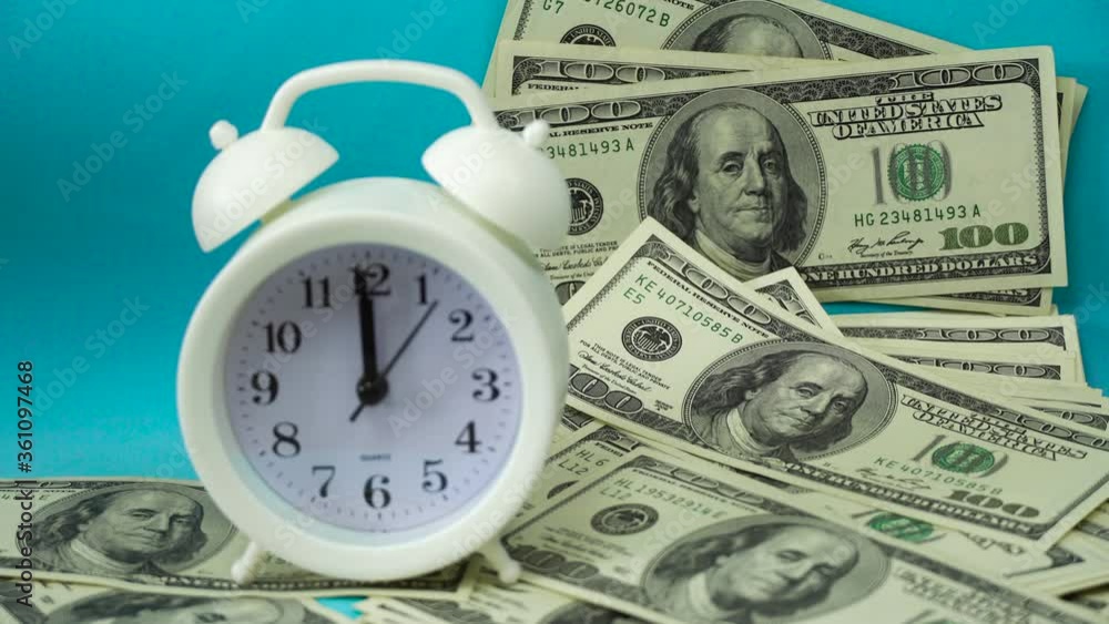 Alarm clock on the background of a lot of hundred-dollar bills, the focus shifts from the alarm clock to banknotes. The concept of Time and money. Alarm clock on the background of a lot of hundred-dollar bills, the focus shifts from the alarm clock to banknotes. The concept of Time and money.