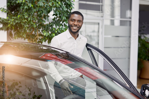 Billede på lærred portrait of happy handsome african man in car dealership, afro man came to buy beautiful luxurious auto