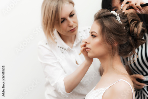morning preparations for the bride s wedding in a beauty salon. A makeup artist does make-up and a hairdresser does her hair