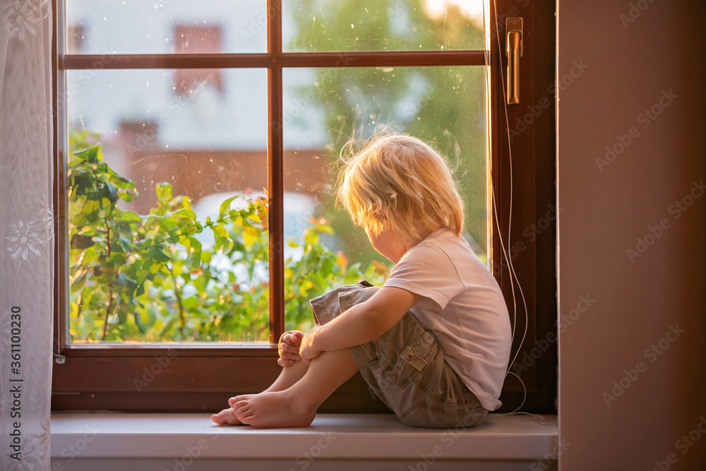 Abandoned little toddler boy, sitting sad on a window shield, looking outside at sunset Abandoned little toddler boy, sitting sad on a window shield, looking outside at sunset
