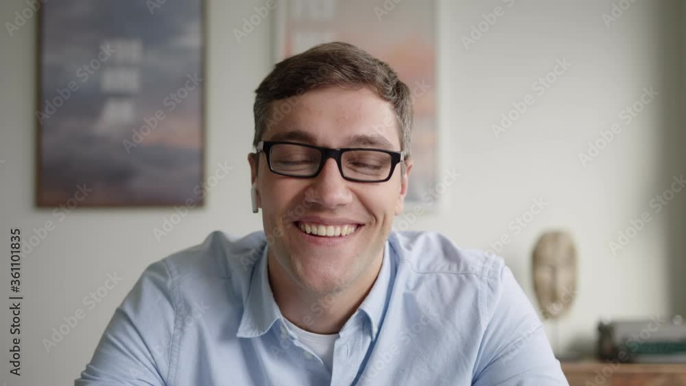 young romantic man with dark hair in glasses and blue shirt sits at table with laptop indoors. uses web camera for video call with girlfriend. gesticulates, blow kisses, smiles. web camera view young romantic man with dark hair in glasses and blue shirt sits at table with laptop indoors. uses web camera for video call with girlfriend. gesticulates, blow kisses, smiles. web camera view