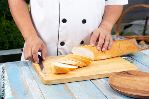 Chef holding knife cutting slide bread making on wooden board