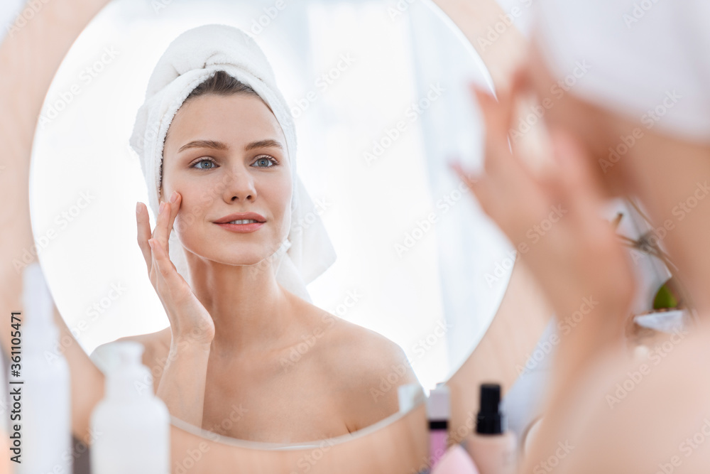 Beautiful young woman looking at mirror and touching her face Beautiful young woman looking at mirror and touching her face