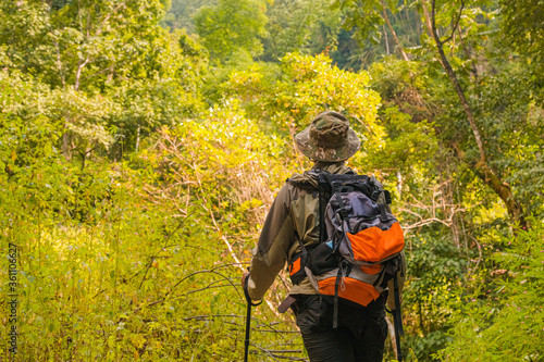 The young man raised with a backpack and mountaineering poles standing in the mountains in the summer outdoors.