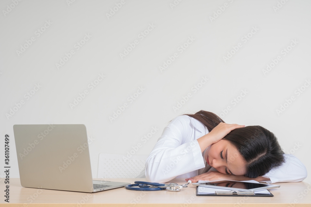 Young Asian woman doctor sitting on desk, she look unhappy and tired because of overwork, Concept of stressed exhausted and doctor liability, Dealing with frustrated Young Asian woman doctor sitting on desk, she look unhappy and tired because of overwork, Concept of stressed exhausted and doctor liability, Dealing with frustrated
