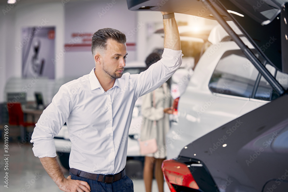 handsome caucasian businessman is examining a car before buying it, he checks all characteristics and features of auto handsome caucasian businessman is examining a car before buying it, he checks all characteristics and features of auto