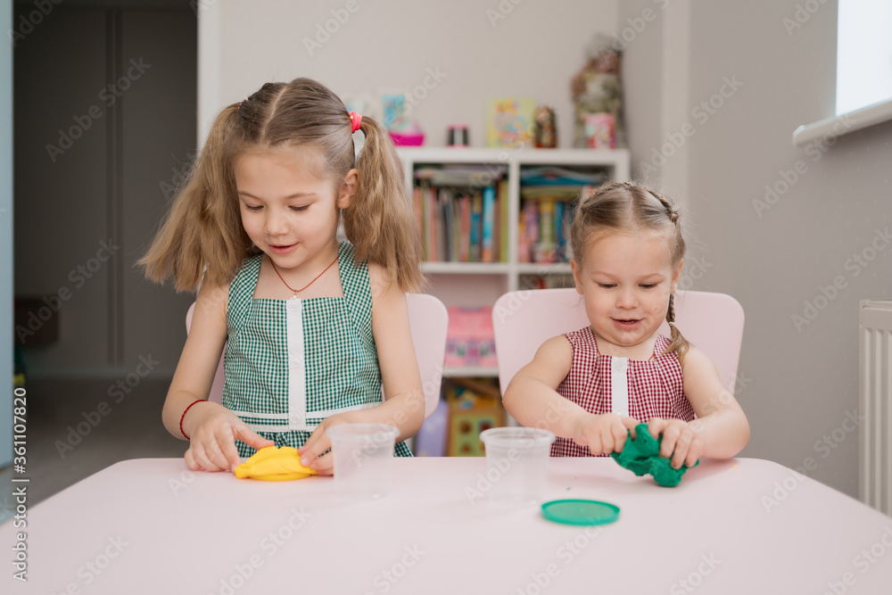 Fototapeta premium Little girls with lovely faces play with clay molding shapes, learning through playing with colored plasticine developing creativity