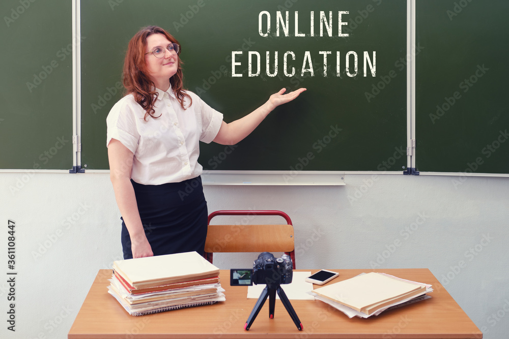A female teacher conducts online training standing in the classroom and shooting videos on a camera. School education via the Internet due to the coronavirus pandemic, copy space A female teacher conducts online training standing in the classroom and shooting videos on a camera. School education via the Internet due to the coronavirus pandemic, copy space