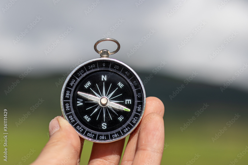 Hand holding a compass with natural blurred green background.. - travel and transportation concept. Hand holding a compass with natural blurred green background.. - travel and transportation concept.