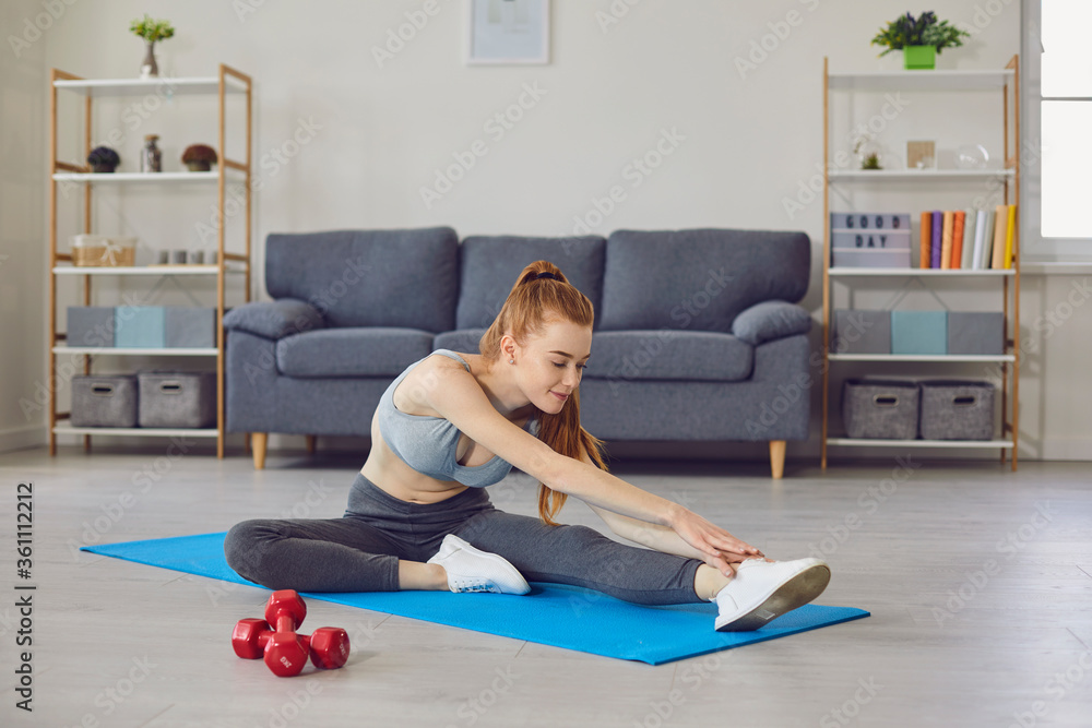 Home sports. Beautiful girl stretching her legs on yoga mat indoors. Flexible young woman working out in living room Home sports. Beautiful girl stretching her legs on yoga mat indoors. Flexible young woman working out in living room