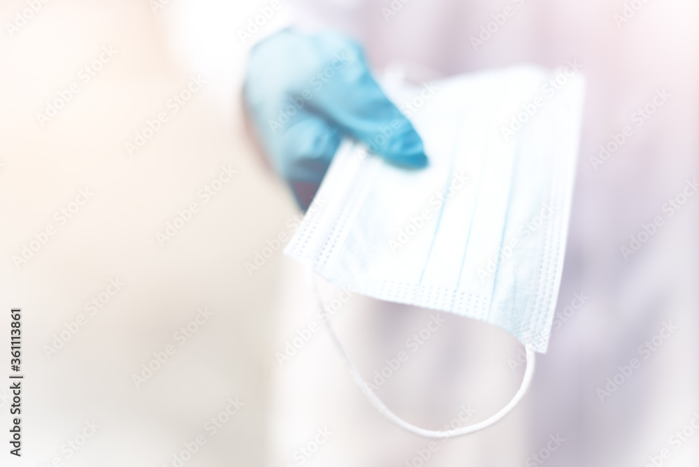 The hands of a doctor or scientist wearing rubber latex gloves extending the surgical face mask to the front of camera. The hands of a doctor or scientist wearing rubber latex gloves extending the surgical face mask to the front of camera.