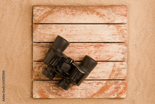 black binoculars monitoring beaches, on a background of rustic wood and sand