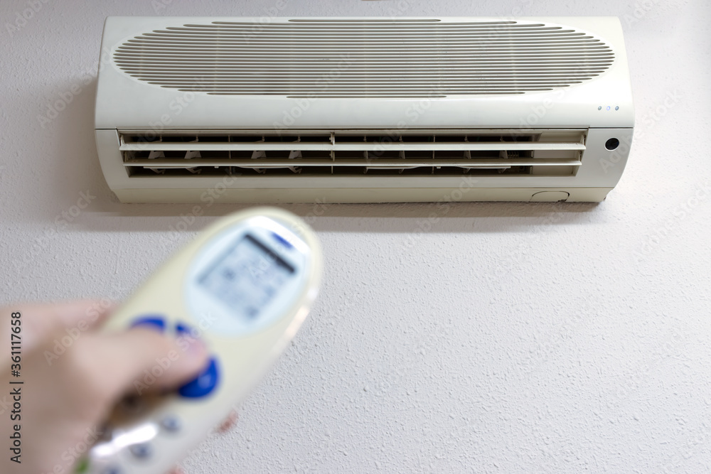 Man's hand holds a remote control directed on the air conditioner, with the remote control turns on the air conditioner Man's hand holds a remote control directed on the air conditioner, with the remote control turns on the air conditioner
