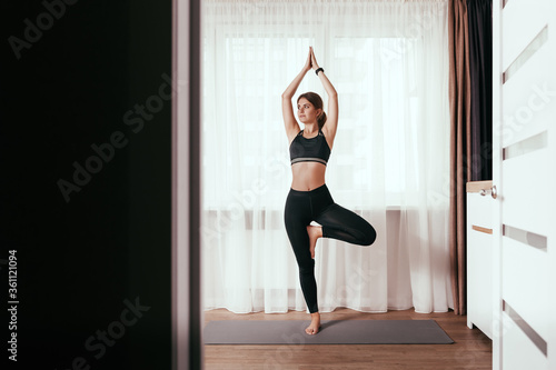 Young girl doing yoga at home in a tree pose. Vrikshasana, namaste. Healthy lifestyle concept photo