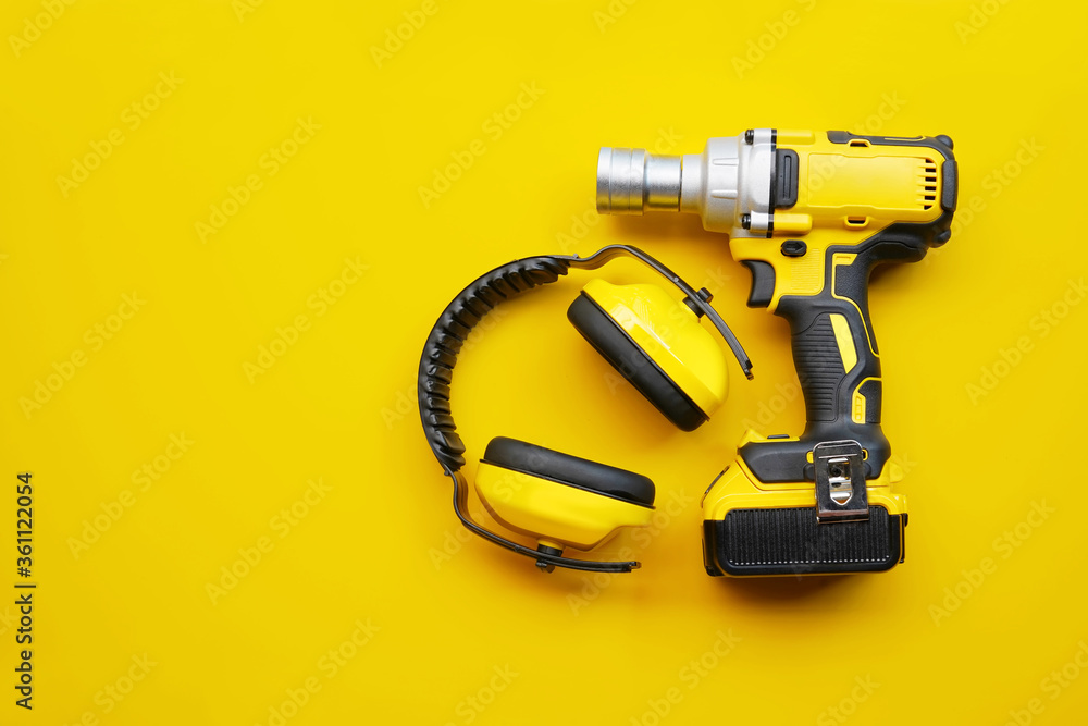 power tools,Ear Muffs, Mid-Range Cordless Impact Wrench on yellow background .Safety Equipment concept . power tools,Ear Muffs, Mid-Range Cordless Impact Wrench on yellow background .Safety Equipment concept .