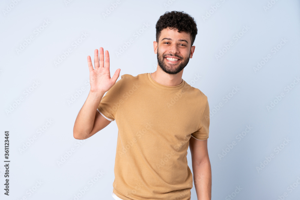 Young Moroccan man isolated on blue background saluting with hand with happy expression Young Moroccan man isolated on blue background saluting with hand with happy expression