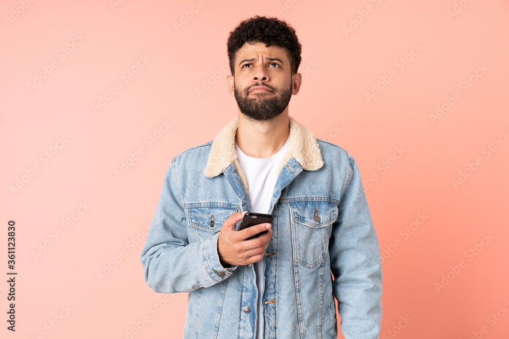Young Moroccan man using mobile phone isolated on pink background and looking up Young Moroccan man using mobile phone isolated on pink background and looking up