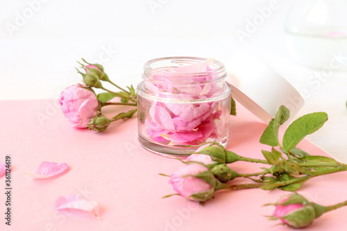 A jar with rose petals, rose blossoms and scattered petals on a pastel background, close-up, side view - the concept of skin care