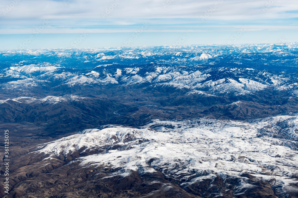 Aerial View of Idaho mountains from the sky while inside an airplane. View of brown mountains and trees covered with snow