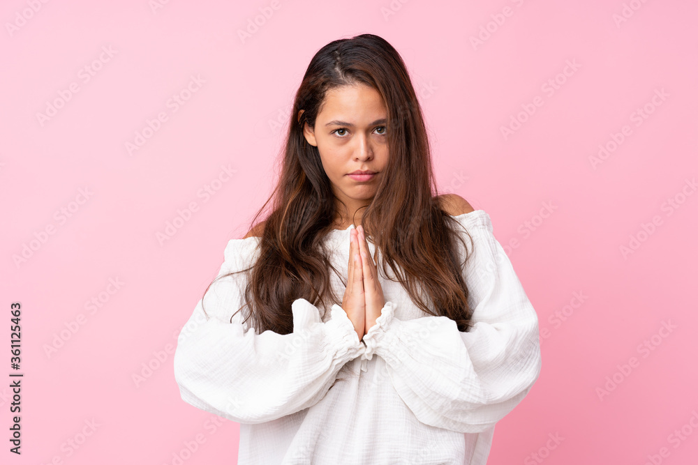 Young Brazilian girl over isolated pink background keeps palm together. Person asks for something Young Brazilian girl over isolated pink background keeps palm together. Person asks for something