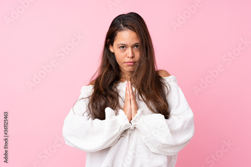 Young Brazilian girl over isolated pink background keeps palm together. Person asks for something © luismolinero