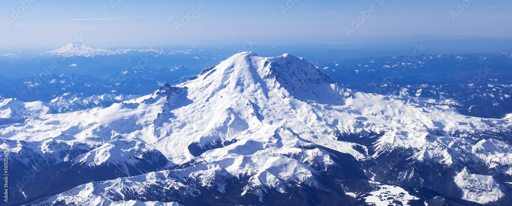 Fototapeta premium Aerial View of Idaho mountains from the sky while inside an airplane. View of brown mountains and trees covered with snow