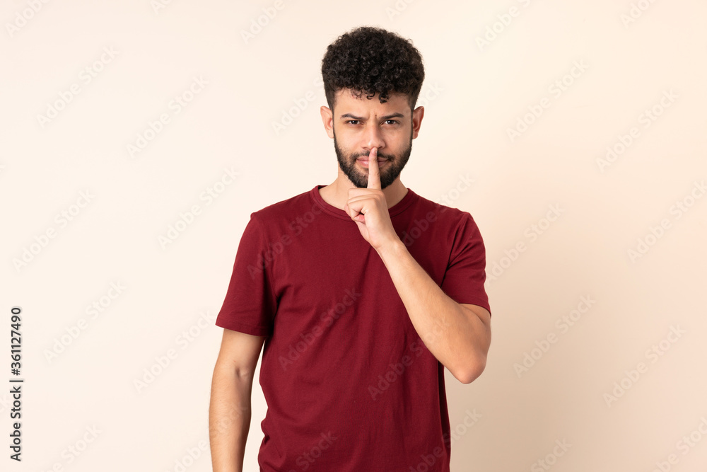 Young Moroccan man isolated on beige background showing a sign of silence gesture putting finger in mouth Young Moroccan man isolated on beige background showing a sign of silence gesture putting finger in mouth