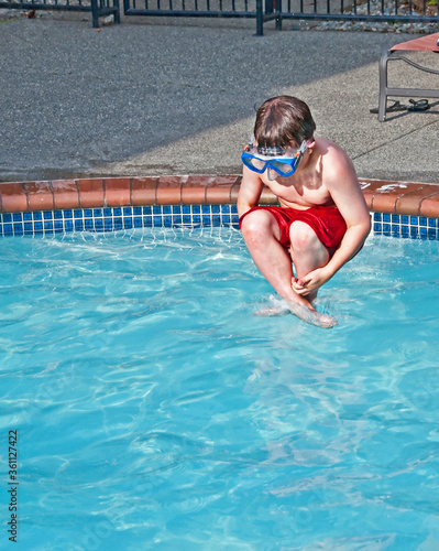 Foto This 7 year old Caucasian boy is wearing a swimming mask, while doing a cannon ball, mid air into a pool of water