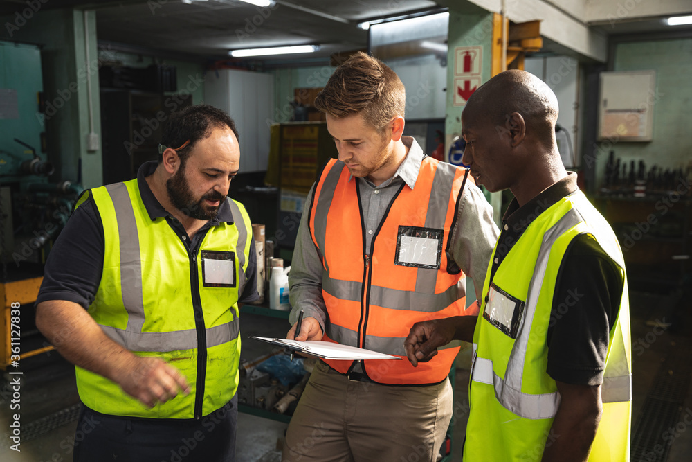 Three male factory workers discussing over a clipboard at the factory Three male factory workers discussing over a clipboard at the factory