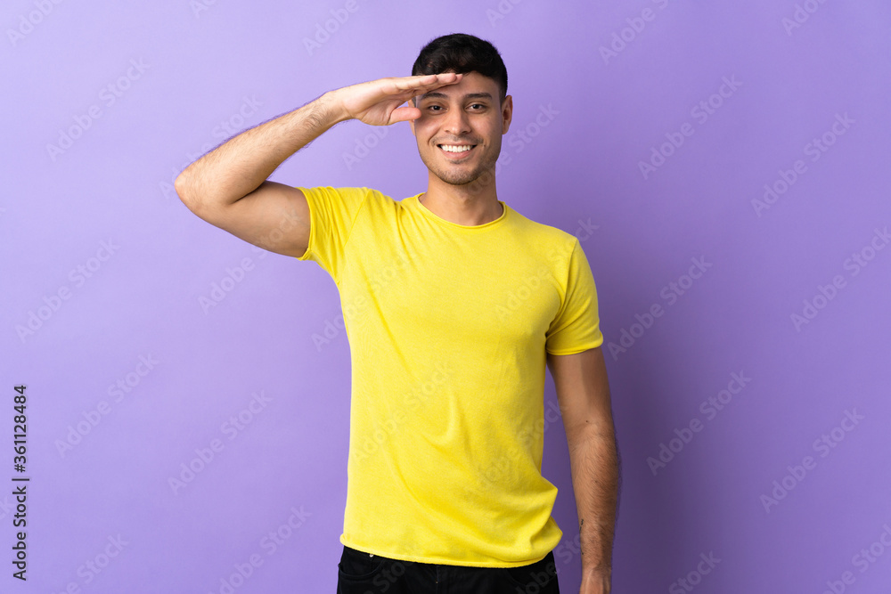 Young Colombian man isolated on purple background saluting with hand with happy expression Young Colombian man isolated on purple background saluting with hand with happy expression
