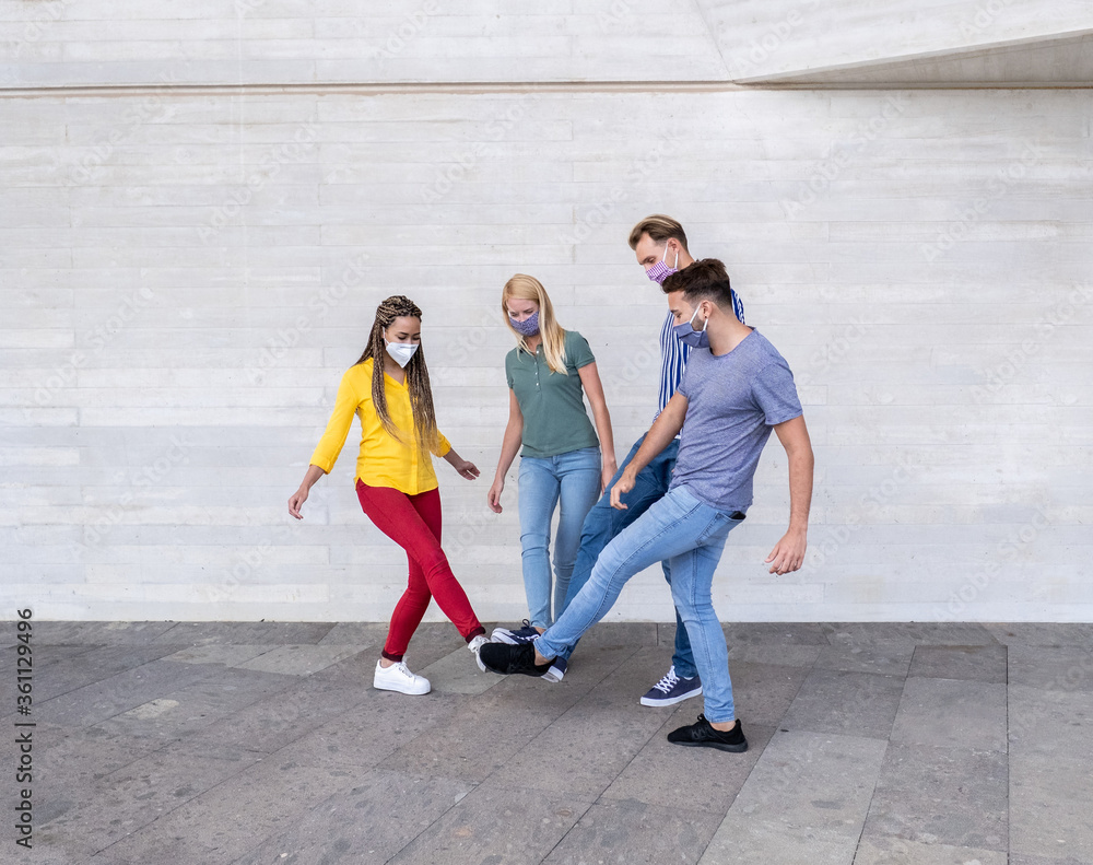 Fototapeta premium Group of young friends meet and greet each other with their feet - Multiracial people wearing face masks - Concept of social distance and health care