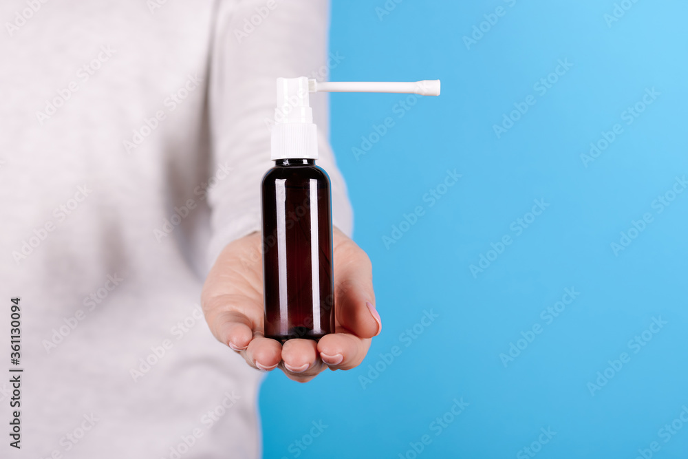 Throat spray bottle in hand on blue background. Close up photo. Throat spray bottle in hand on blue background. Close up photo.